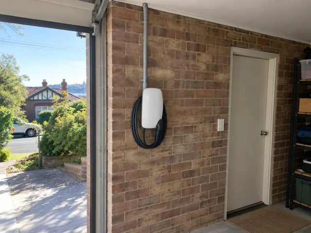 EV charger mounted on a brick garage wall beside a door and open driveway in Fairlight
